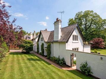 White-rendered house with a gabled roof and tall chimney, seen across a striped lawn